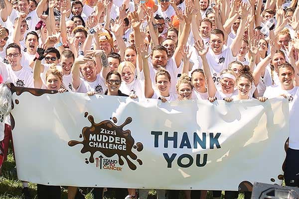 Large group of people with their hands in the air and holding a thank you sign for the mudder challenge.